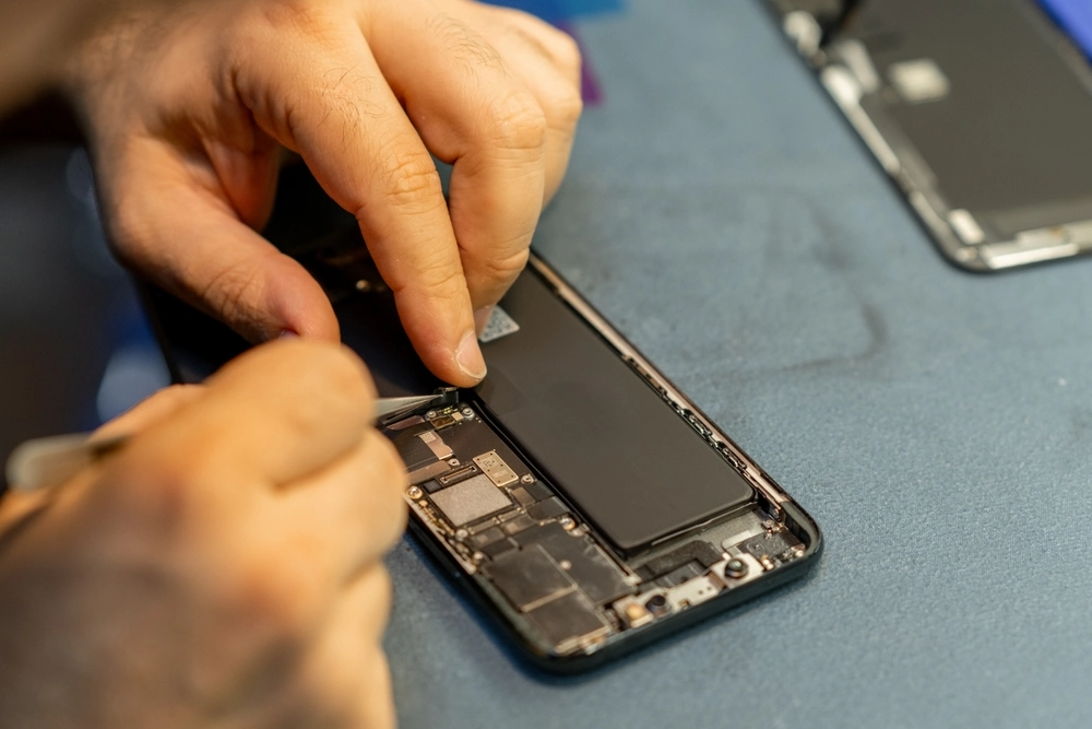 Technician repairing a smartphone battery and internal components.